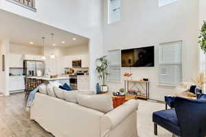 Living room featuring a towering ceiling, sink, and light wood-type flooring