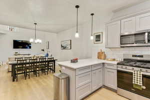 Kitchen featuring tasteful backsplash, stainless steel appliances, decorative light fixtures, and kitchen peninsula