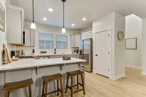 Kitchen with a breakfast bar area, appliances with stainless steel finishes, tasteful backsplash, decorative light fixtures, and light wood-type flooring