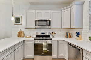 Kitchen featuring pendant lighting, stainless steel appliances, decorative backsplash, and white cabinets