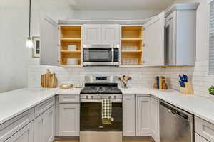 Kitchen featuring white cabinetry, decorative light fixtures, stainless steel appliances, and decorative backsplash