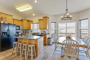 Kitchen featuring light hardwood / wood-style flooring, black appliances, a kitchen island, decorative backsplash, and vaulted ceiling