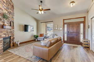 Living room featuring lofted ceiling, a fireplace, light hardwood / wood-style floors, and ceiling fan