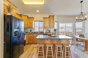 Kitchen featuring black fridge with ice dispenser, sink, light wood-type flooring, a kitchen island, and stove