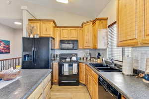 Kitchen featuring vaulted ceiling, sink, decorative backsplash, light hardwood / wood-style floors, and black appliances