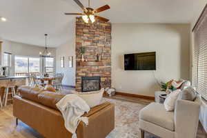 Living room with high vaulted ceiling, a stone fireplace, ceiling fan with notable chandelier, and light hardwood / wood-style flooring