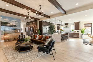 Living room with beamed ceiling, light hardwood / wood-style flooring, and a notable chandelier