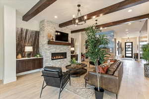 Living room featuring beamed ceiling, a stone fireplace, and light hardwood / wood-style flooring