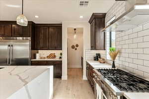 Kitchen with stovetop, decorative light fixtures, stainless steel built in fridge, light stone countertops, and wall chimney range hood