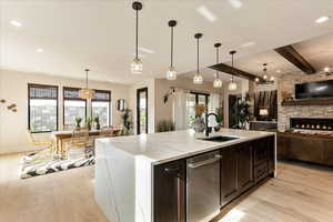 Kitchen featuring pendant lighting, a kitchen island with sink, sink, and light stone counters