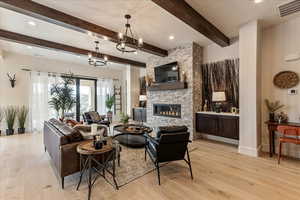 Living room with an inviting chandelier, beam ceiling, a fireplace, and light hardwood / wood-style floors