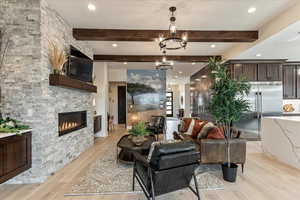 Living room with a notable chandelier, beam ceiling, a fireplace, and light hardwood / wood-style floors