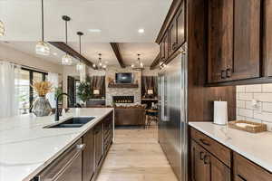 Kitchen with a fireplace, sink, hanging light fixtures, stainless steel appliances, and light stone countertops