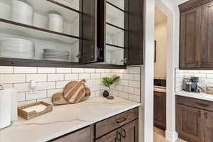 Bar with tasteful backsplash, dark brown cabinets, and light stone counters