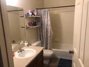 Full bathroom with vanity, wood-type flooring, shower / tub combo with curtain, and toilet