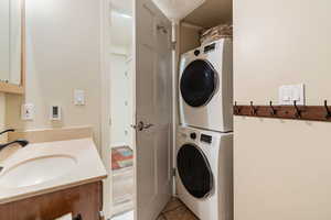 Clothes washing area featuring light tile patterned flooring, stacked washer and clothes dryer, and sink