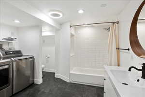 Full bathroom featuring washing machine and dryer, vanity, shower / tub combo with curtain, and toilet