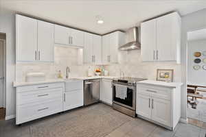 Kitchen with appliances with stainless steel finishes, wall chimney exhaust hood, sink, and white cabinets