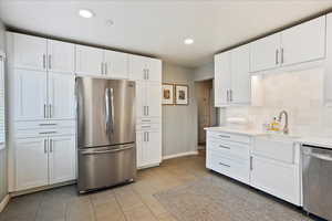 Kitchen featuring sink, white cabinets, backsplash, light tile patterned floors, and stainless steel appliances