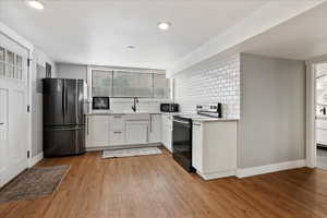 Kitchen with white cabinets, stainless steel fridge, decorative backsplash, electric range, and light hardwood / wood-style flooring