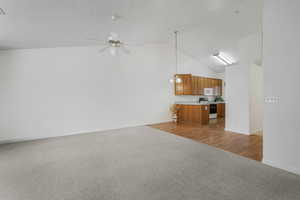 Unfurnished living room featuring light carpet, a textured ceiling, high vaulted ceiling, and ceiling fan