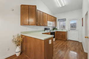 Kitchen with sink, wood-type flooring, vaulted ceiling, kitchen peninsula, and white appliances