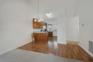 Kitchen featuring pendant lighting, high vaulted ceiling, dark hardwood / wood-style floors, a notable chandelier, and kitchen peninsula