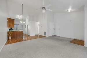 Unfurnished living room featuring ceiling fan with notable chandelier, light colored carpet, sink, and high vaulted ceiling