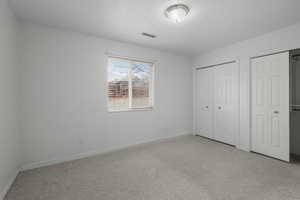 Unfurnished bedroom featuring multiple closets, light carpet, and a textured ceiling