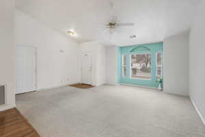 Spare room with ceiling fan, carpet flooring, vaulted ceiling, and a textured ceiling