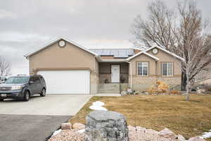 Ranch-style home featuring a garage, a front lawn, and solar panels