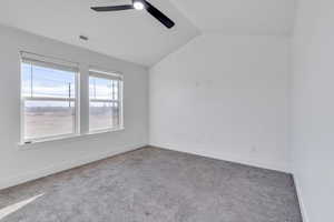 Carpeted empty room featuring ceiling fan and vaulted ceiling