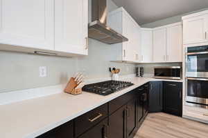 Kitchen featuring white cabinetry, appliances with stainless steel finishes, wall chimney range hood, and light hardwood / wood-style floors