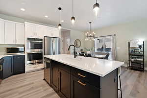 Kitchen featuring decorative light fixtures, sink, a kitchen island with sink, stainless steel appliances, and light hardwood / wood-style flooring