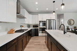 Kitchen with wall chimney range hood, stainless steel appliances, hanging light fixtures, and white cabinets