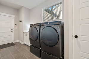 Clothes washing area featuring separate washer and dryer, tile patterned flooring, and cabinets