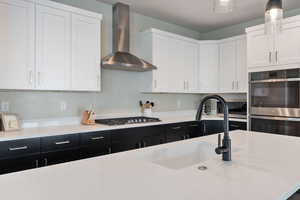 Kitchen featuring wall chimney exhaust hood, sink, white cabinetry, hanging light fixtures, and stainless steel appliances