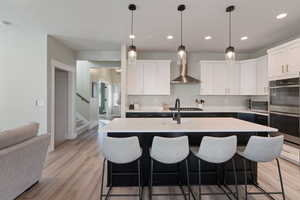 Kitchen featuring white cabinetry, wall chimney range hood, a kitchen island with sink, and stainless steel appliances