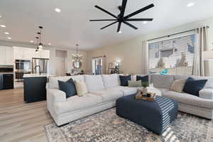 Living room featuring light hardwood / wood-style flooring, ceiling fan with notable chandelier, and a wealth of natural light