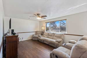 Living room featuring ceiling fan, dark wood-type flooring, and fresh paint.