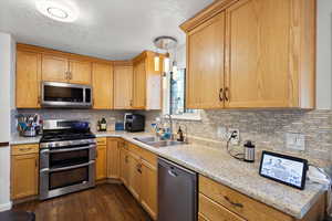 Kitchen with dark wood-type flooring, sink, light stone counters, tasteful backsplash, and stainless steel appliances