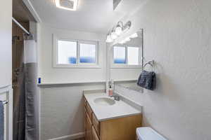 UPdated bathroom featuring walk in shower, vanity, toilet, and a textured ceiling