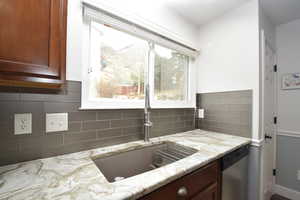 Kitchen with stainless steel dishwasher, light stone countertops, sink, and backsplash