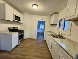 Kitchen featuring white appliances, a sink, white cabinets, light countertops, and light wood finished floors