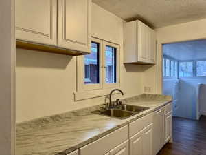 Kitchen with dark wood-style floors, white cabinetry, a sink, a textured ceiling, and dishwasher