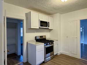 Kitchen with white microwave, white cabinets, light countertops, stainless steel gas range, and dark wood-style floors