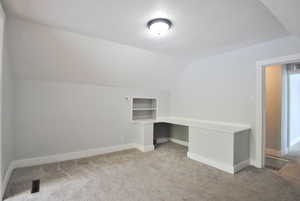 Additional living space with built in desk, lofted ceiling, light carpet, and a textured ceiling