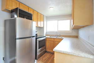 Kitchen featuring sink, wood-type flooring, a textured ceiling, light brown cabinets, and stainless steel appliances