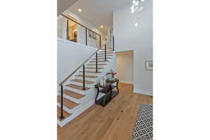 Staircase with an inviting chandelier, wood-type flooring, and a high ceiling