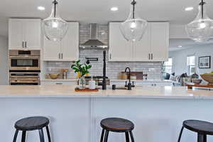 Kitchen with pendant lighting, wall chimney exhaust hood, and white cabinets